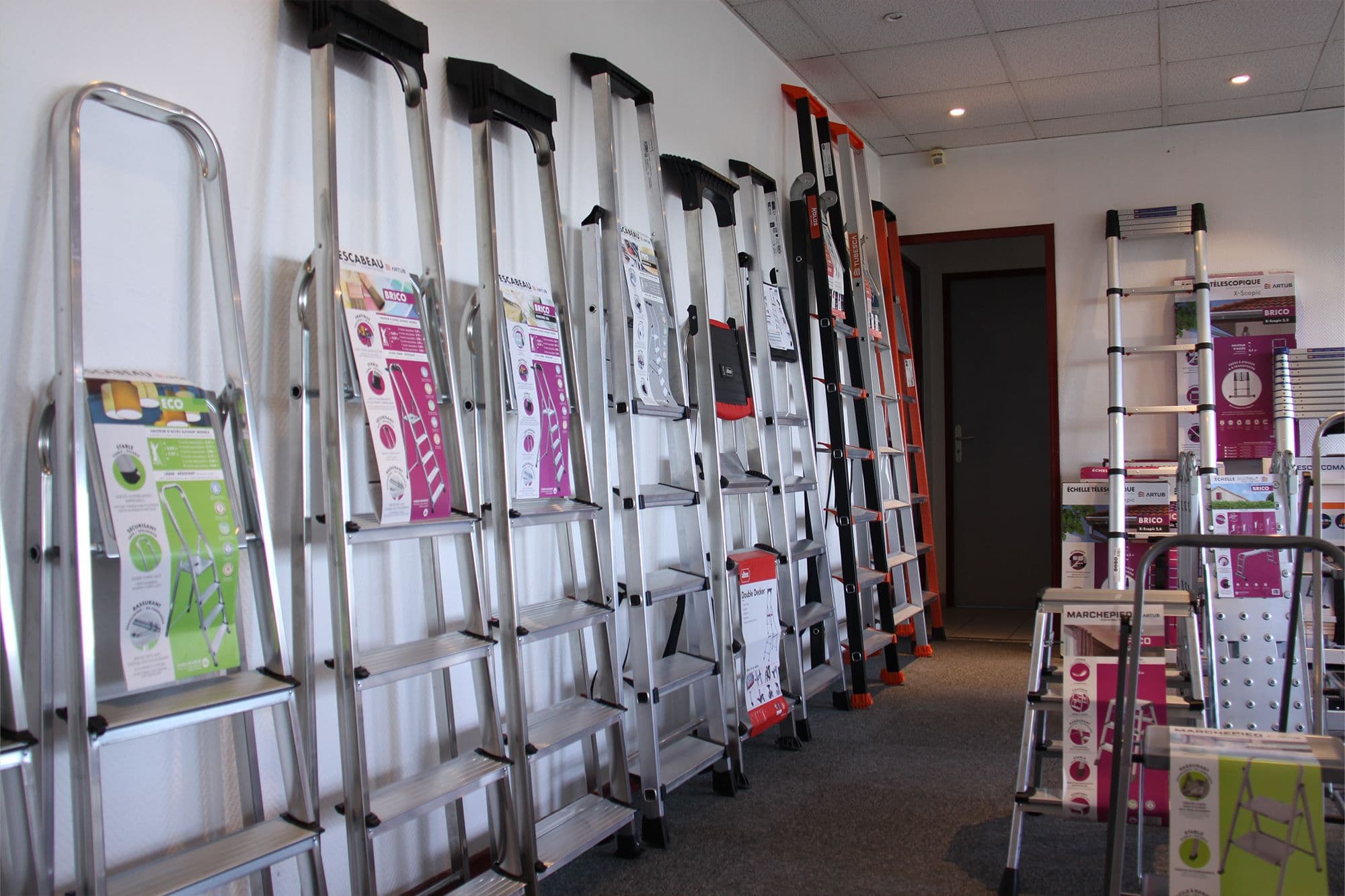 Various aluminum ladders displayed in a store aisle, showcasing different sizes and designs for sale.