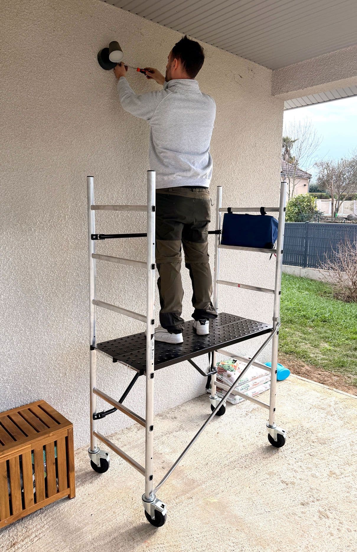 Man on mobile scaffold applies plaster to an exterior white wall with a roller.